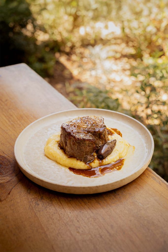 Close-up of a seared beef fillet served on a bed of creamy purée with a rich jus, photographed outdoors at Bodega Binafadet, Menorca. Captured by Lou Carruthers, hospitality and food photographer.