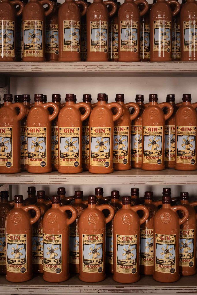 Rows of terracotta bottles of Xoriguer gin neatly arranged on shelves at Destilería Xoriguer, Menorca, showcasing the island’s local spirit. Photographed by Lou Carruthers, hospitality and food photographer.