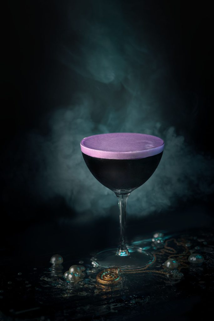 Purple Ursula-inspired cocktail with teal atmospheric lighting, creative drinks photographer Lou Carruthers UK