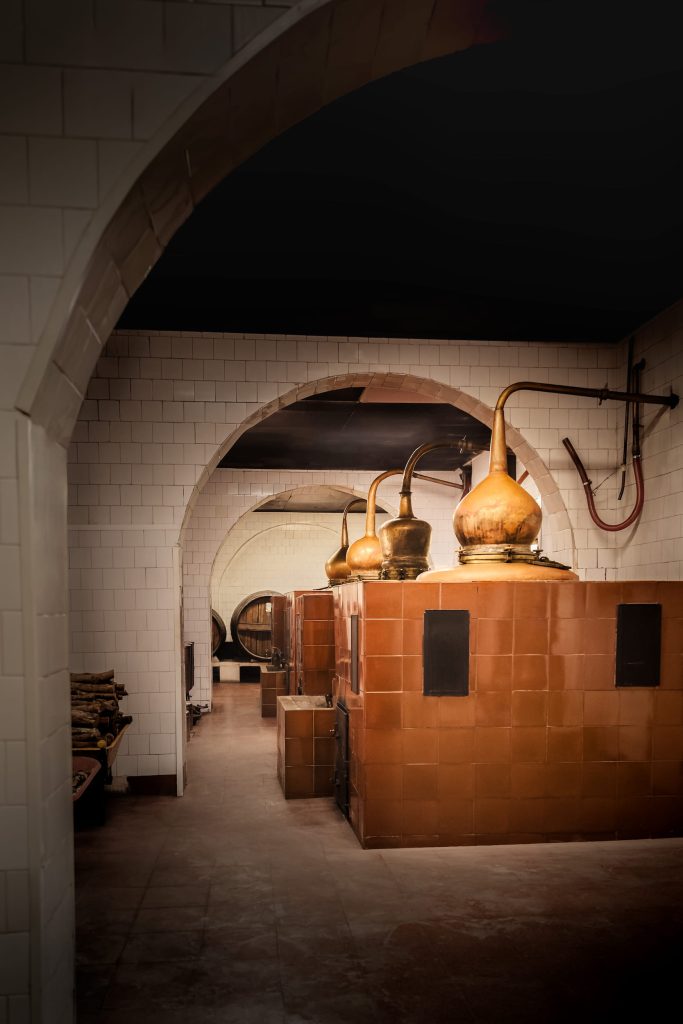 Wood-fired copper stills inside Xoriguer distillery, burnished with age and tradition, used weekly to distil Mahón gin. Photographed by Lou Carruthers, food and hospitality photographer.