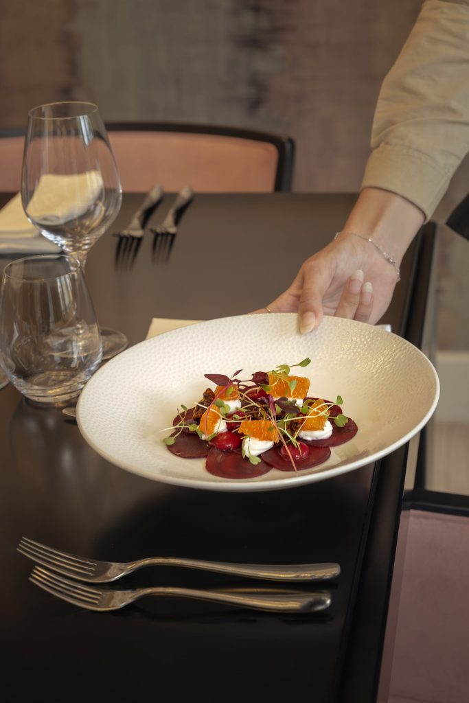 Staff member presenting a colourful beetroot, orange and goats’ cheese salad at The Orangery, Siddington Park, captured in a refined restaurant setting.