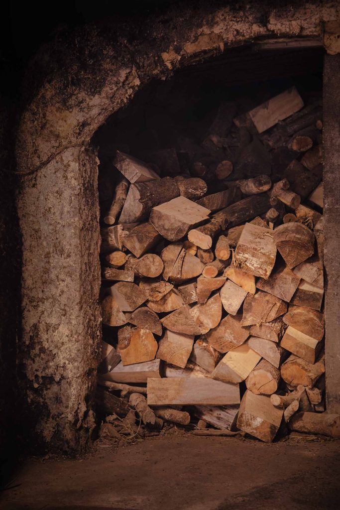 A stone alcove filled with stacked firewood, ready to fuel the copper stills during the gin-making process. Photographed by Lou Carruthers, food and hospitality photographer.
