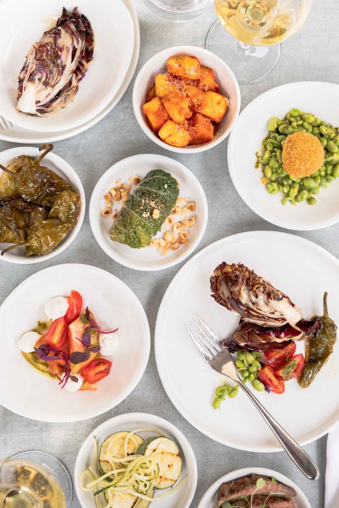 Mediterranean-inspired table spread featuring grilled fish, roasted potatoes, fresh salads, and vibrant vegetable dishes, styled for a relaxed outdoor dining experience. Photographed by Lou Carruthers, hospitality and food photographer.