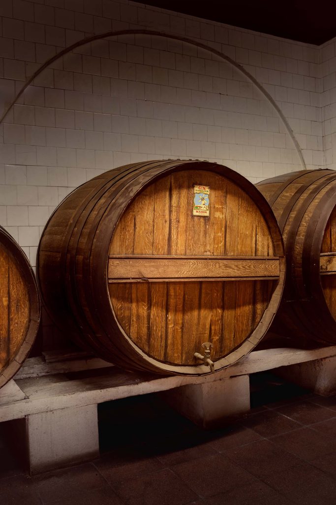 Large wooden barrels in the cool cellar of Xoriguer distillery, waiting to store and mature the freshly distilled gin. Photographed by Lou Carruthers, food and hospitality photographer.