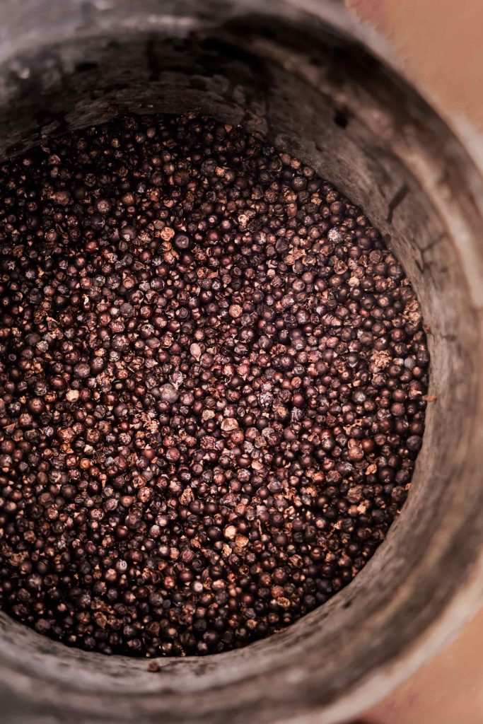 A close-up view of wild juniper berries inside a rustic wooden bucket, rich in texture and earthy tones. Photography by Lou Carruthers. Photographed by Lou Carruthers, food and hospitality photographer.