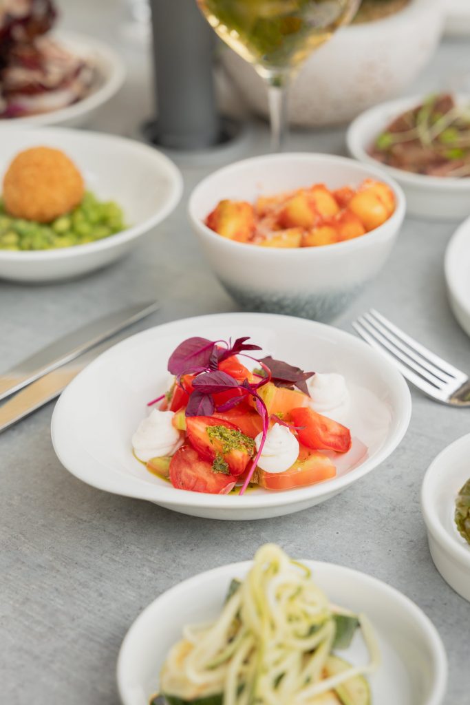 lose-up of a fresh tomato and mozzarella small plate with basil oil and micro herbs at Siddington Park, styled as part of an outdoor dining experience