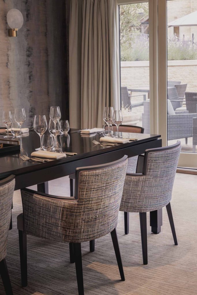 Elegant private dining room set with polished black table, neatly arranged glassware, and upholstered chairs, overlooking an outdoor terrace through large windows. Photographed by Lou Carruthers, hospitality and food photographer.
