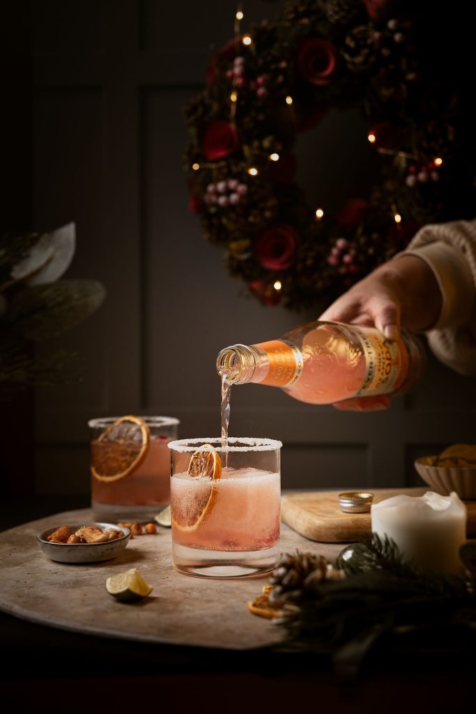 Festive Paloma cocktail being poured with Fever-Tree Pink Grapefruit Soda, garnished with dried orange and served on a winter-themed table setting by Lou Carruthers Photography