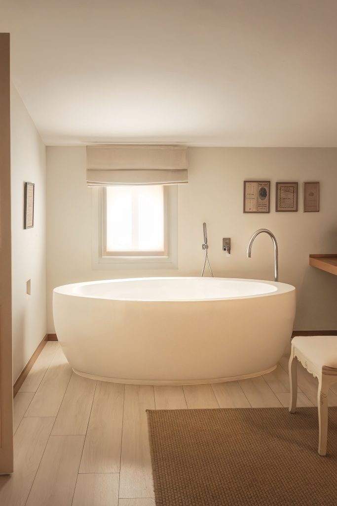Bathroom at Jardí de Ses Bruixes boutique hotel in Menorca, featuring a freestanding white bath, pale wood floor, warm neutral tones and soft natural light.