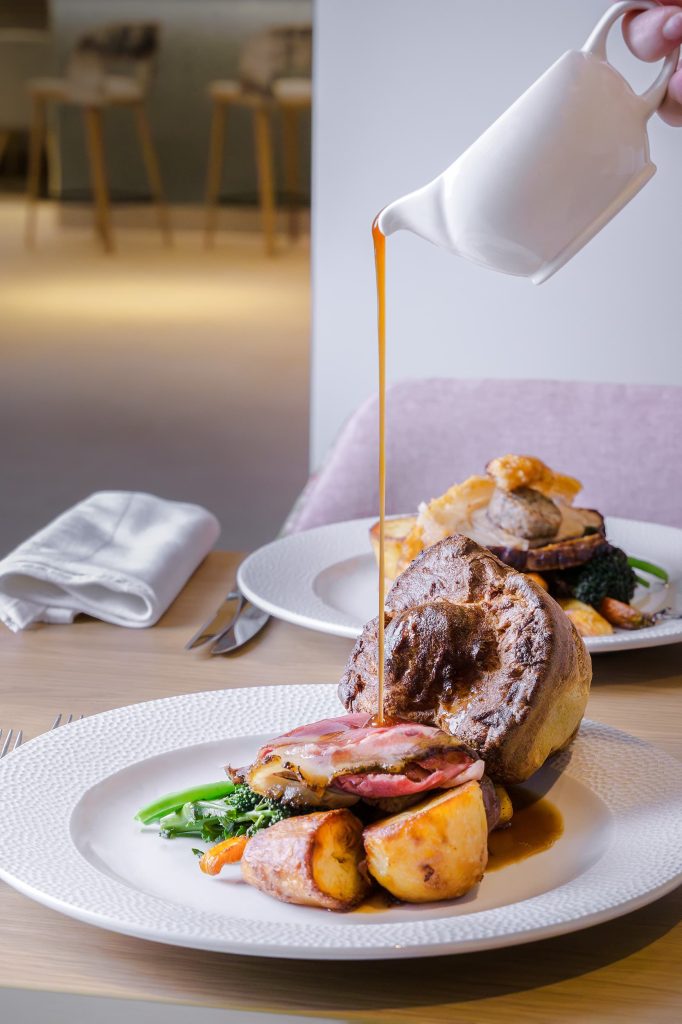 Roast beef served with seasonal vegetables and crisp roast potatoes, finished with rich jus being poured at the table at Siddington Park, photographed by Lou Carruthers, Lou Carruthers Photography, Hospitality & Drinks Photographer, Cotswolds and Menorca